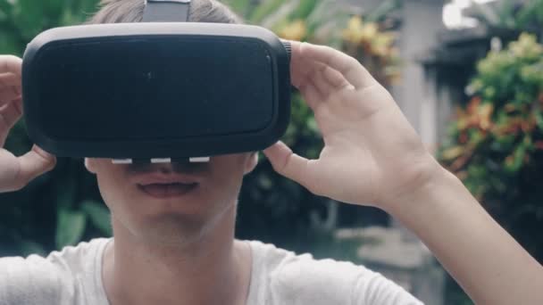 Närbild porträtt av ung man använder en virtual reality-glasögon utomhus på garden — Stockvideo