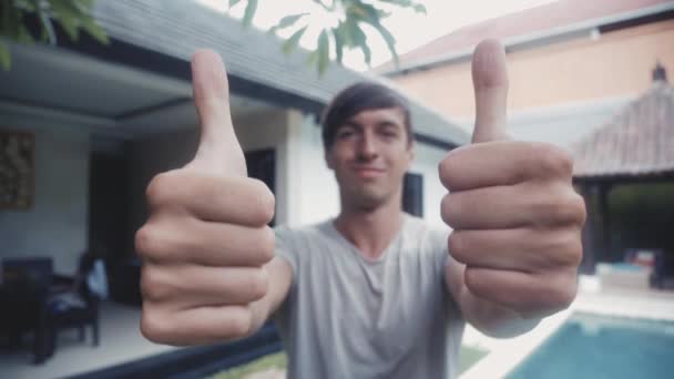 Šťastný mladý muž dávat dva palce a usmívá se venkovní před domem. — Stock video