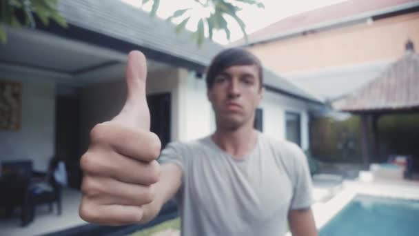 Щасливий молодий чоловік дає великий палець і посміхається на відкритому повітрі у дворі — стокове відео