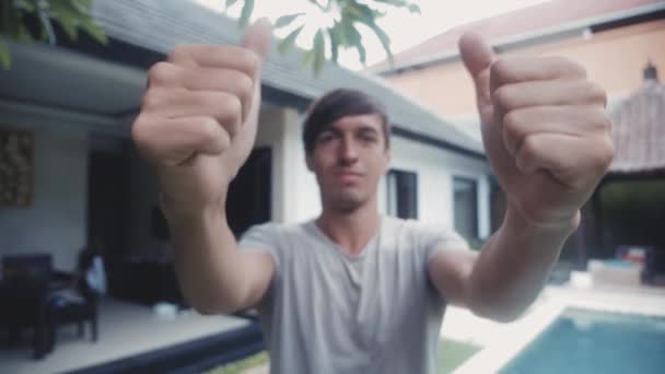 幸せな若い男 2 つの親指をあきらめて、家の前に屋外の笑みを浮かべて. — ストック動画