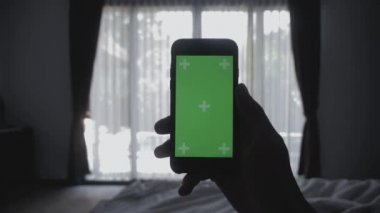 Genç adam otantik sosyal medya paylaşımı smartphone yeşil ekran chroma anahtar yeşil ekran tutan yatakta döşeme kapatın