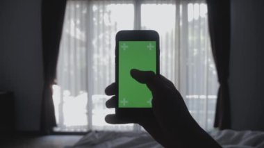 Genç adam otantik sosyal medya paylaşımı smartphone yeşil ekran chroma anahtar yeşil ekran tutan yatakta döşeme kapatın
