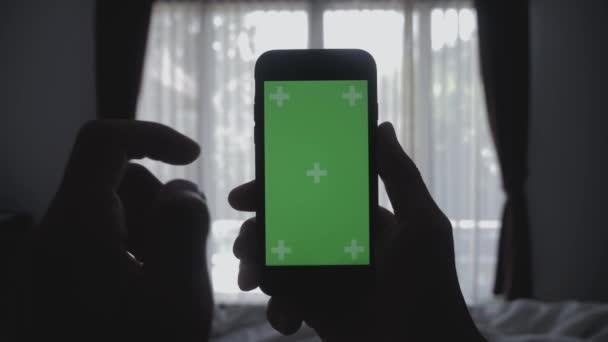 Закрыть Молодой человек лежит на кровати, держа смартфон зеленый экран хрома-ключ зеленый экран обмена подлинными социальными сетями — стоковое видео