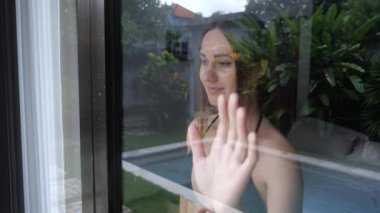 Kadın pencereden dışarı bakar ve elini sallayarak birine elveda diyor. 4k, ağır çekim.