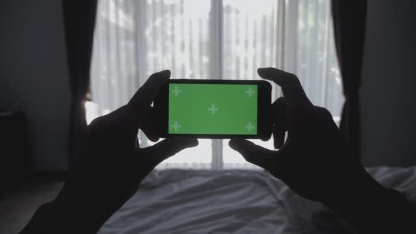 Крупним планом Молодий чоловік лежить на ліжку тримає смартфон зелений екран хром-ключ зелений екран, ділячись справжніми соціальними медіа — стокове відео