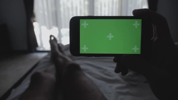 Close up Giovane uomo sdraiato sul letto con smartphone schermo verde chroma-key greenscreen condivisione di autentici social media — Video Stock