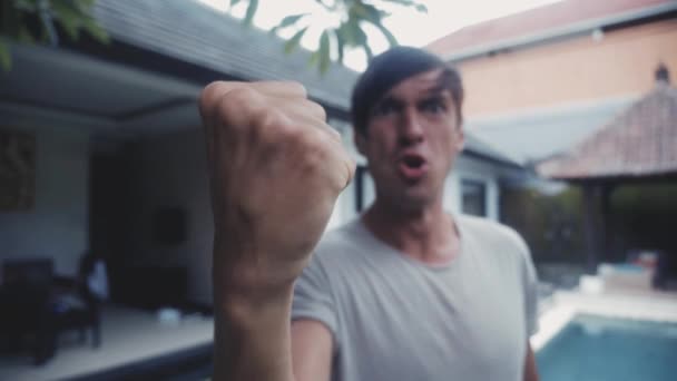 Agressieve man schreeuwt en bedreigt met een vuist tegen de achtergrond van het huis in zijn tuin. Dreiging met geweld — Stockvideo