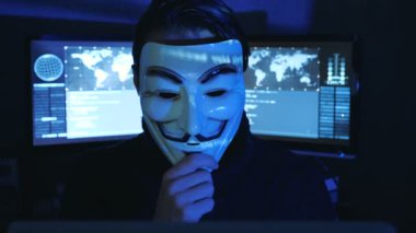 Cherkassy, Ukrayna, 04 Ocak 2019: Hacker gizler yüzünü karanlık odada Guy Fawkes maskesi arkasında dolu ekranları görüntülemek.