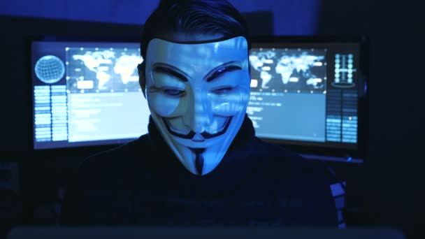 Cherkassy, Ukraine, January 04 2019: Hacker hides his face behind the mask of Guy Fawkes in dark room filled with display screens. — Stock Video