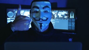 Cherkassy, Ukrayna, 04 Ocak 2019: Hacker Anonim Guy Fawkes maskesi içinde başparmak karanlık oda göstermek perde ile dolu görünür.