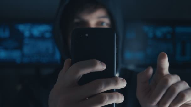 Farliga Hacker i huven använder en smartphone i en hemlig datacenter fylld med skärmar — Stockvideo