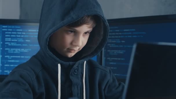 データ センター内のコンピューターに取り組んでいるフードの若き天才少年ハッカー プログラマは画面に満ちています 子供の天才ハッカーの肖像画 — ストック動画