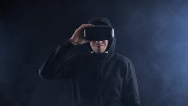 Uomo futuristico col cappuccio con auricolare VR. Uomo futuristico che utilizza occhiali di realtà virtuale in una stanza fumosa scura . — Video Stock