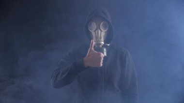 Gaz maskesi ve başparmak gösterilmesini dumanlı karanlık yere kukuleta adam portresi. Onay kavramı.