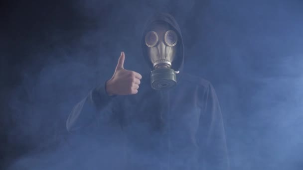 가스 마스크와 후드 엄지손가락을 보여주는 연기가 자욱한 어두운 장소에 있는 남자의 초상화. 승인 개념. — 비디오