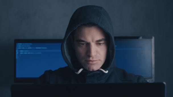 Розшукуваний чоловік хакер в капоті працює на комп'ютері в темній офісній кімнаті — стокове відео