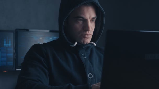Концепция киберпреступлений. Хакер в капюшоне работает за компьютером в темной офисной комнате — стоковое видео