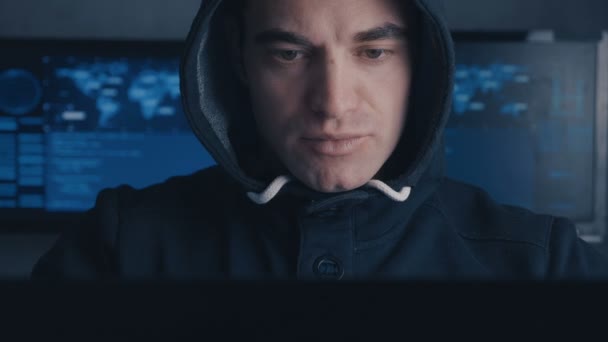 Крупный план хакера в капюшоне, работающего за компьютером в темной офисной комнате — стоковое видео