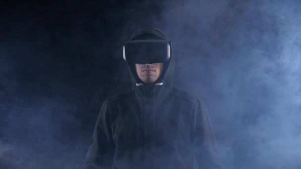 Futurisztikus ember hood Vr fülhallgatót visel. Futurisztikus ember használja a virtuális valóság szemüveg a sötét füstös szobában. — Stock videók