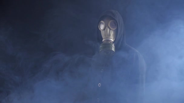Человек в противогазе и капюшоне в дыму в темном месте — стоковое видео