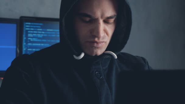 Handsome Male hacker in hood working on a computer in a dark office room. Shot on steadicam — Stock Video