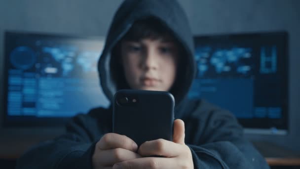 Молодий з капюшоном хакер дитина, використовуючи смартфон пристрій для викрадення. Геній хлопчик дивує системою хакерів в кіберпросторі . — стокове відео