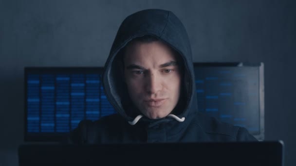 Розшукуваний чоловік хакер в капоті працює на комп'ютері в темній офісній кімнаті — стокове відео