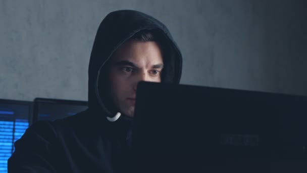 Wanted Hacker in hood working on a computer in a dark office room. Shot on steadicam — Stock Video