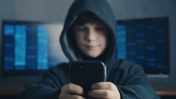 フード付きのスマート フォンのデバイスを使用して少年の若い。天才天才少年の肖像画は、サイバー スペースでシステムをハッキングします。. — ストック動画