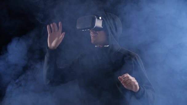Homem jovem em óculos VR ou fone de ouvido virtual em local escuro fumegante. Novas tecnologias e realidade aumentada . — Vídeo de Stock