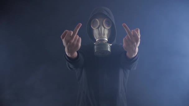 Człowiek w masce gazowej pokazuje środkowy palec w zadymionej ciemnym pokoju. — Wideo stockowe