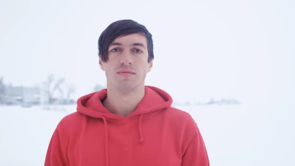 Schöner junger Mann sieht Kamera im Winter schneereich kalt im Freien — Stockvideo