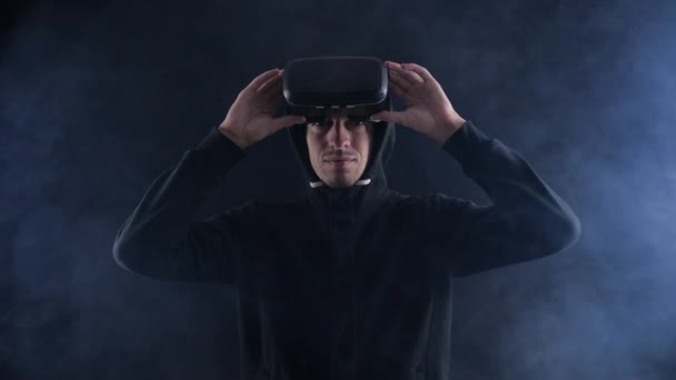 Uomo futuristico col cappuccio con auricolare VR. Uomo futuristico che utilizza occhiali di realtà virtuale in una stanza fumosa scura . — Video Stock