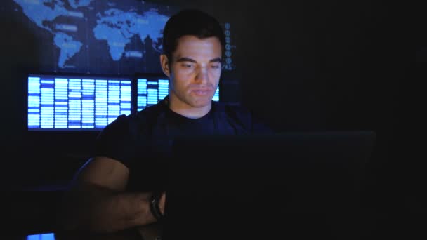 Guapo programador hacker masculino trabaja en una computadora por la noche en un centro de datos lleno de pantallas de monitor — Vídeos de Stock