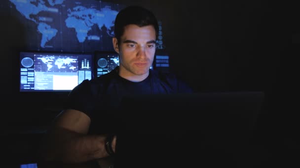 Красивий чоловічий хакер-програміст працює за комп'ютером вночі в центрі обробки даних, наповненому екранами монітора — стокове відео