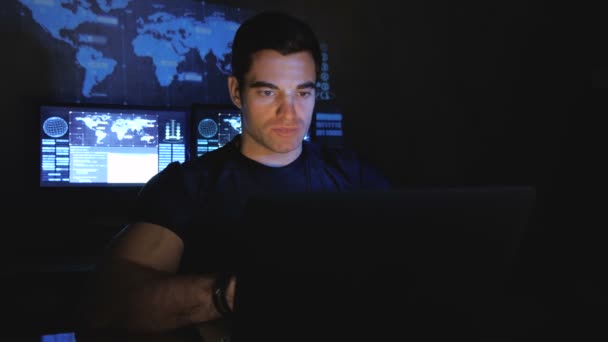 Guapo programador hacker masculino trabaja en una computadora por la noche en un centro de datos lleno de pantallas de monitor — Vídeos de Stock