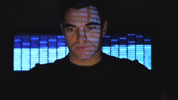 Hombre atractivo hacker trabaja en una computadora por la noche en la oficina en un centro de datos, mientras que los personajes de código azul reflejan en su cara por la noche en la habitación de la oficina . — Vídeo de stock