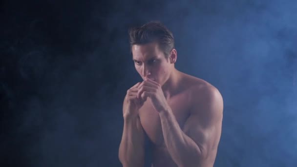 Atleta boxeador dando socos com um olhar intenso em seu rosto no fundo escuro fumegante — Vídeo de Stock