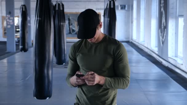 Atleta comprueba Smartphone mientras hace ejercicio. Hombre joven escribiendo descanso durante el entrenamiento en el gimnasio — Vídeo de stock