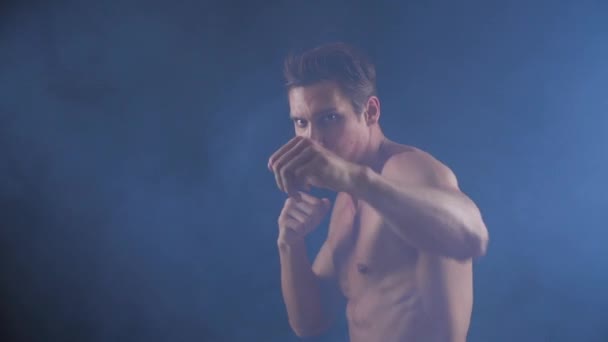 Vechter man met hemd uit kale hij boksen en ponsen op de camera in rook op zwarte achtergrond — Stockvideo