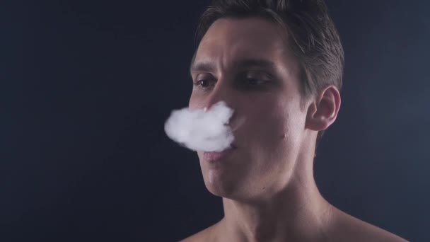 Közelkép jóképű férfi vaper kilégzéskor nagy felhők a füst, az e-cigaretta vape fekete háttér a lassú mozgás