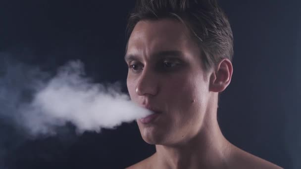 Gros plan bel homme vaper expirer de gros nuages de fumée avec e-cigarette vape sur fond noir au ralenti — Video