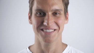 Gülümseyen ve beyaz duvar arka plan üzerinde kameraya bakarak gülümsüyor iyi görünümlü bir adam portresi. Yakın çekim. Kapalı.