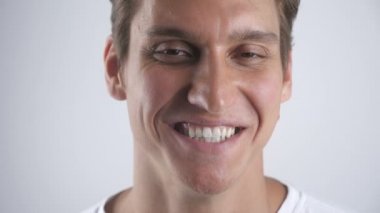 Gülümseyen ve beyaz duvar arka plan üzerinde kameraya bakarak gülümsüyor iyi görünümlü bir adam portresi. Yakın çekim. Kapalı.