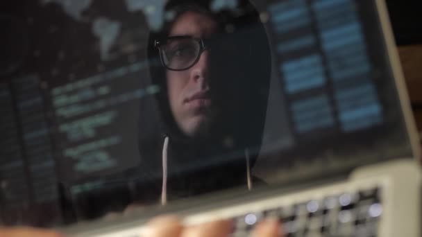 Doppia esposizione: uomo hacker in occhiali che lavora presso un computer portatile. Hacker scrive codice blu, riflessione nel monitor — Video Stock