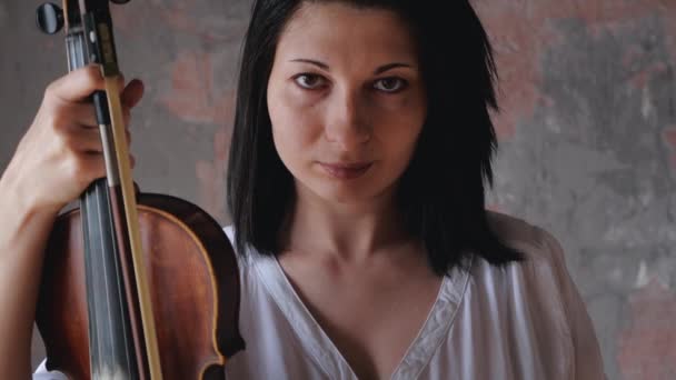 Портрет жінки-музикантки, що тримає скрипку в руках і дивиться на камеру — стокове відео