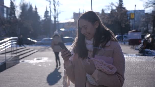 Retrato de mulher morena sorridente vestindo casaco elegante e cachecol, na rua da cidade com digitação de telefone inteligente — Vídeo de Stock