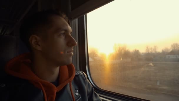 Ο νεαρός έχει ταξίδι με το τρένο. Ο άνθρωπος κοιτάζει έξω από το παράθυρο κατά τη διάρκεια του τρένου στο ηλιοβασίλεμα — Αρχείο Βίντεο