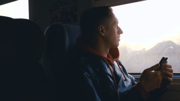 Jovem a fazer uma viagem de comboio. Homem olhando pela janela durante o passeio de trem ao pôr do sol — Vídeo de Stock