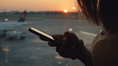 Akıllı telefon kullanarak kadın silüeti. Havaalanında gün batımı veya gündoğumu arka planda mobil ile kadın elleri çekim yakın